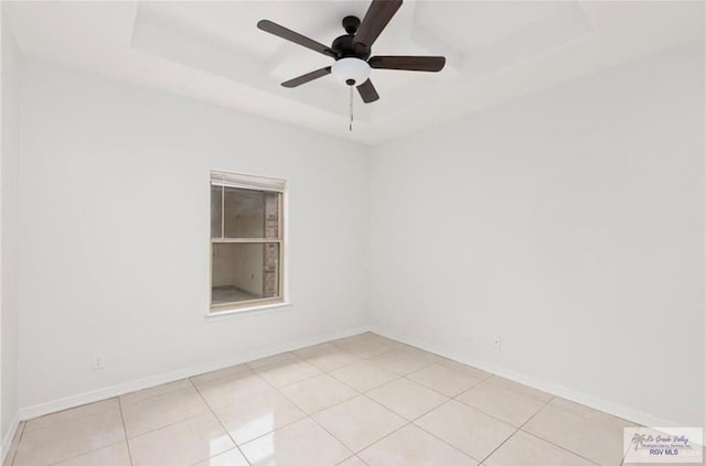 empty room featuring light tile patterned floors, a tray ceiling, and ceiling fan