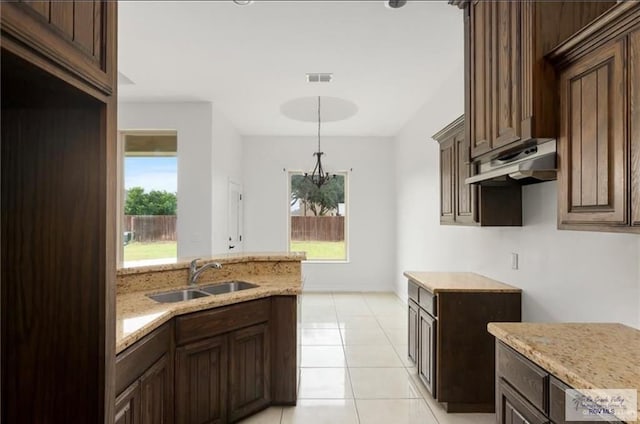 kitchen with light stone countertops, dark brown cabinets, sink, light tile patterned floors, and decorative light fixtures