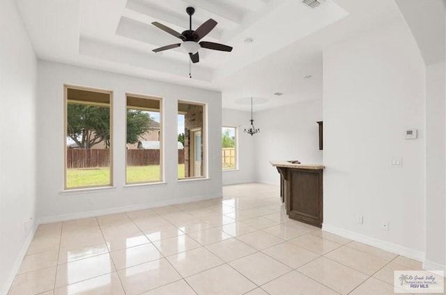 spare room with light tile patterned floors, ceiling fan with notable chandelier, and a tray ceiling