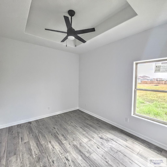 spare room featuring ceiling fan, light wood-type flooring, and a tray ceiling