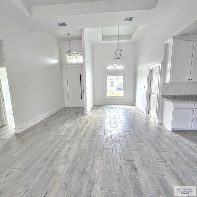 entryway featuring a raised ceiling, an inviting chandelier, a high ceiling, and light wood-type flooring