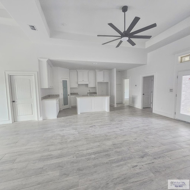 unfurnished living room featuring a tray ceiling, ceiling fan, and light hardwood / wood-style floors