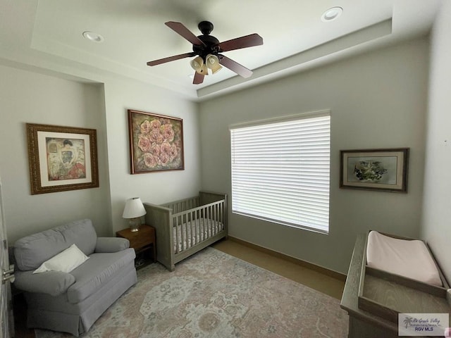 bedroom with a crib, a raised ceiling, recessed lighting, baseboards, and ceiling fan