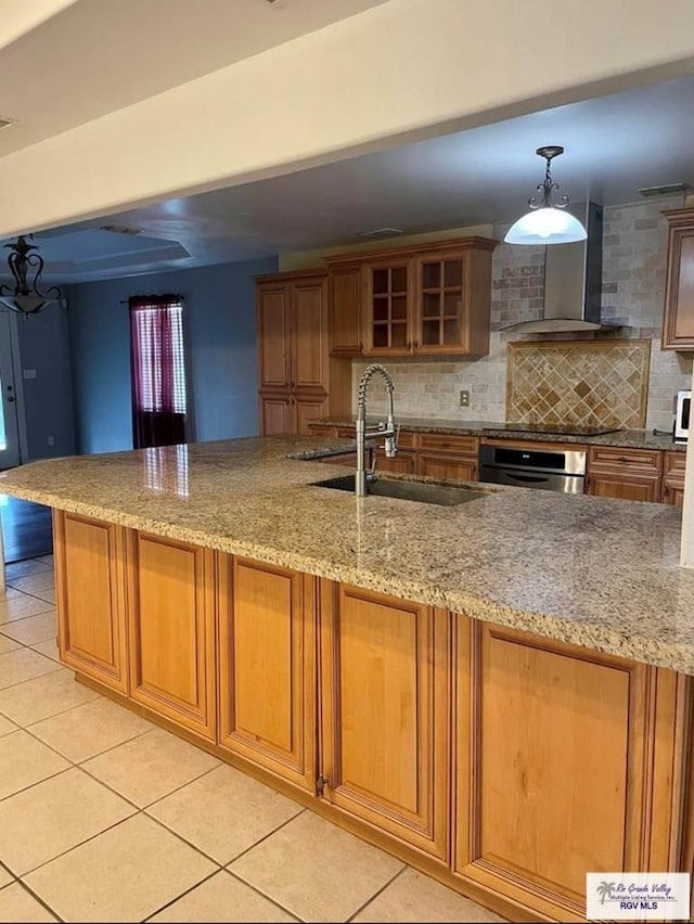 kitchen featuring stainless steel oven, wall chimney range hood, sink, hanging light fixtures, and light tile patterned floors