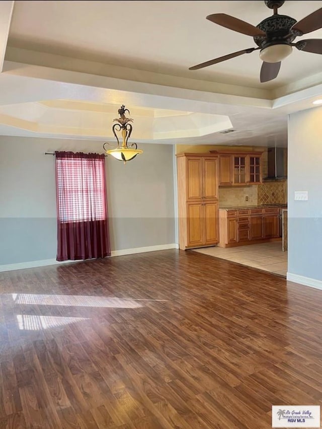 unfurnished living room with hardwood / wood-style floors, ceiling fan, and a raised ceiling