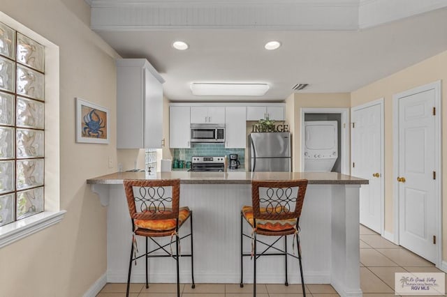 106 Atol St Unit 7, South Padre Island, TX 78597 - kitchen featuring stainless steel appliances, stacked washer / dryer, a peninsula, backsplash, and white cabinetry