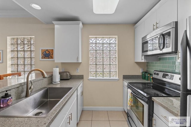 106 Atol St Unit 7, South Padre Island, TX 78597 - kitchen featuring appliances with stainless steel finishes, a sink, baseboards, light tile patterned flooring, and white cabinetry