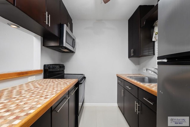 kitchen with butcher block counters, dark brown cabinetry, sink, light tile patterned floors, and appliances with stainless steel finishes