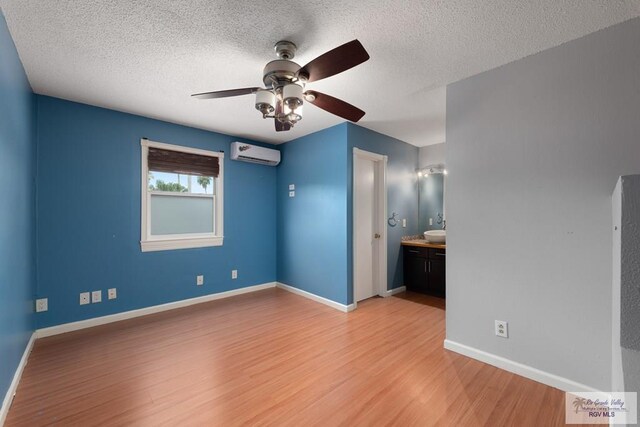 unfurnished bedroom with a wall mounted air conditioner, a textured ceiling, light hardwood / wood-style floors, and ceiling fan