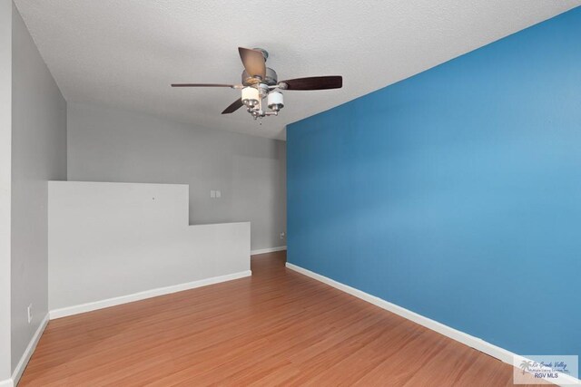 empty room with ceiling fan, wood-type flooring, and a textured ceiling