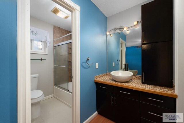 full bathroom with tile patterned flooring, combined bath / shower with glass door, toilet, and vanity