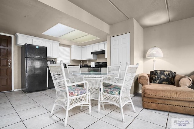 kitchen with light tile patterned floors, a skylight, white cabinetry, and black appliances