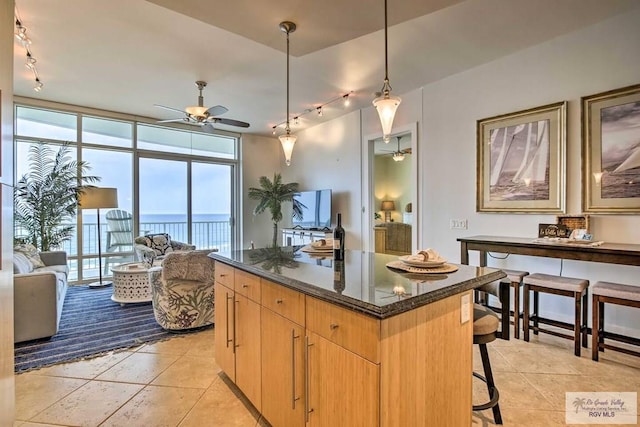 kitchen with a breakfast bar area, a wall of windows, dark stone counters, a kitchen island, and pendant lighting