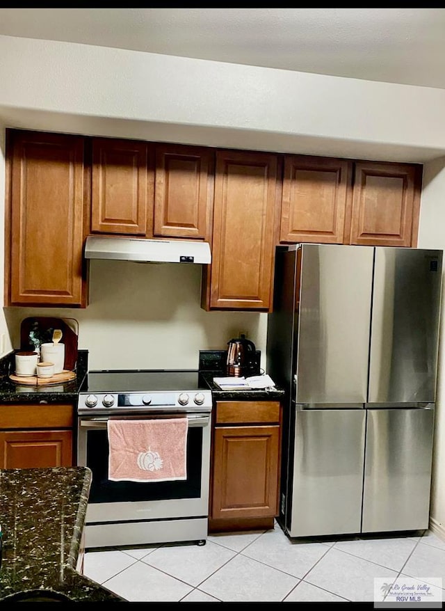 kitchen with stainless steel appliances, light tile patterned flooring, and dark stone countertops