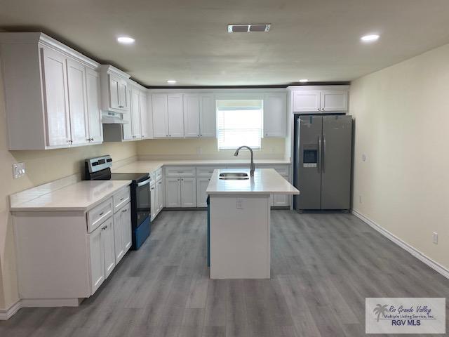 kitchen with a kitchen island with sink, white cabinets, sink, wood-type flooring, and stainless steel appliances