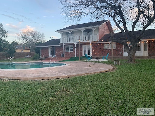 back of property with french doors, a balcony, a lawn, and a patio area