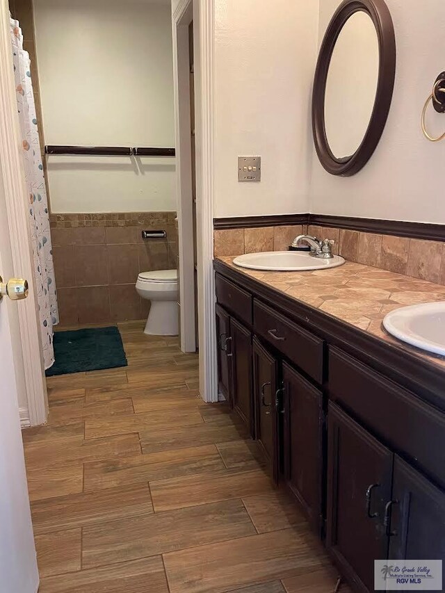 bathroom featuring toilet, vanity, and tile walls