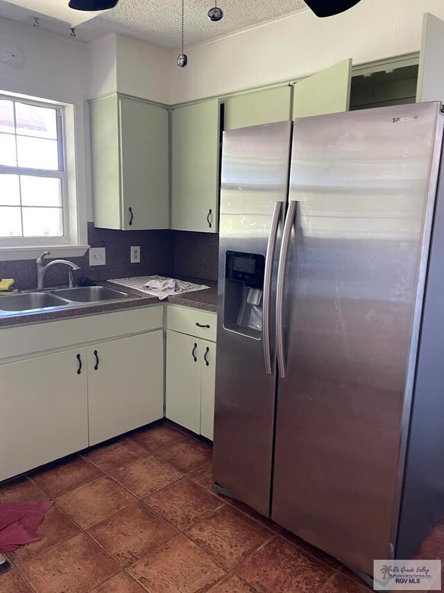 kitchen with stainless steel refrigerator with ice dispenser, sink, white cabinetry, a textured ceiling, and decorative backsplash