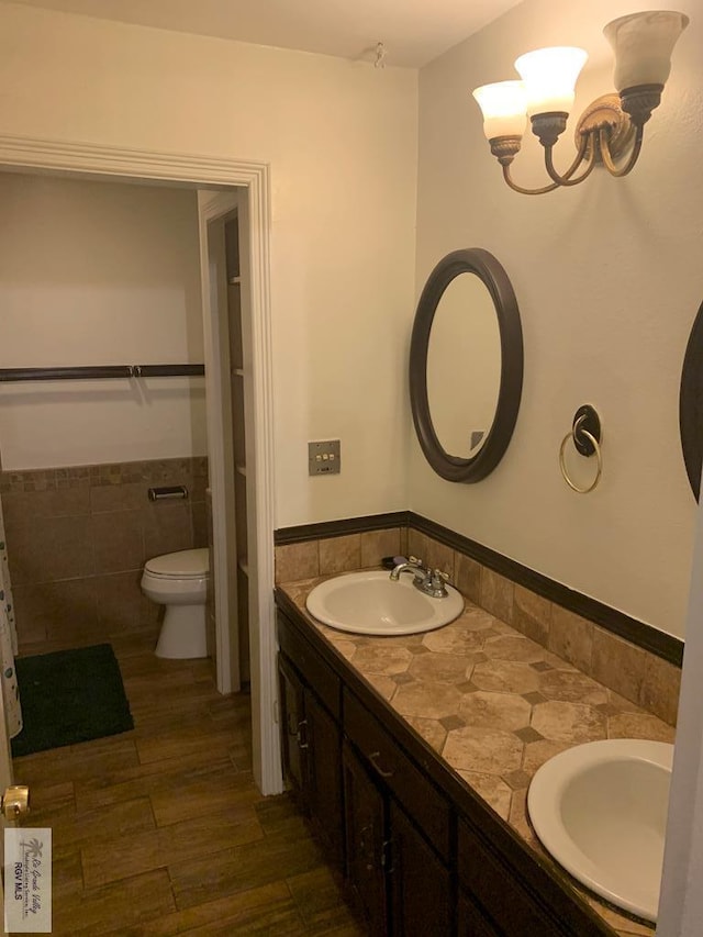 bathroom with toilet, wood-type flooring, a chandelier, tile walls, and vanity