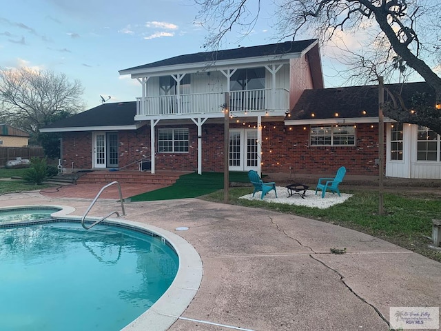 back of property featuring a balcony, a fire pit, a patio area, and a swimming pool with hot tub