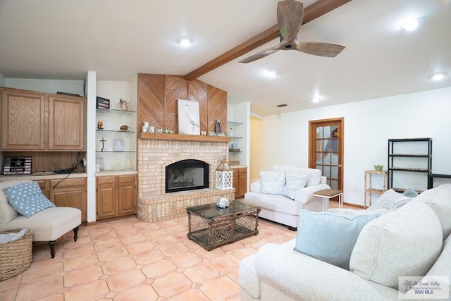 tiled living room with lofted ceiling with beams, ceiling fan, built in features, and a brick fireplace