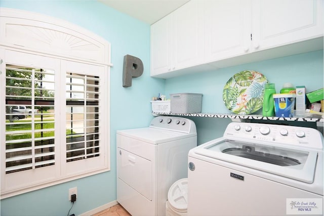 clothes washing area with washing machine and dryer, light tile patterned floors, and cabinets