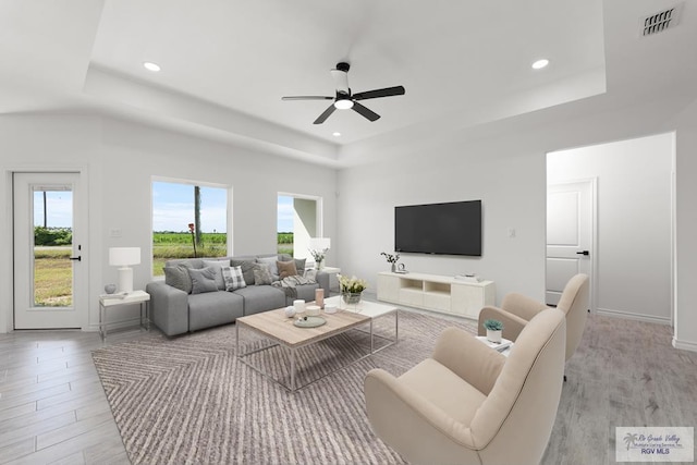 living room featuring ceiling fan, light hardwood / wood-style floors, and a tray ceiling