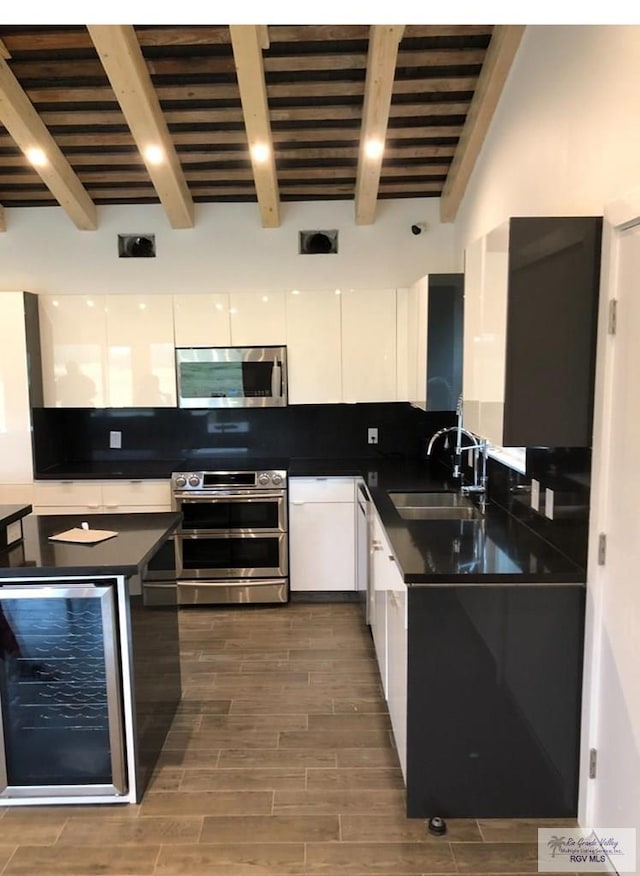 kitchen with stainless steel appliances, white cabinetry, beverage cooler, and sink