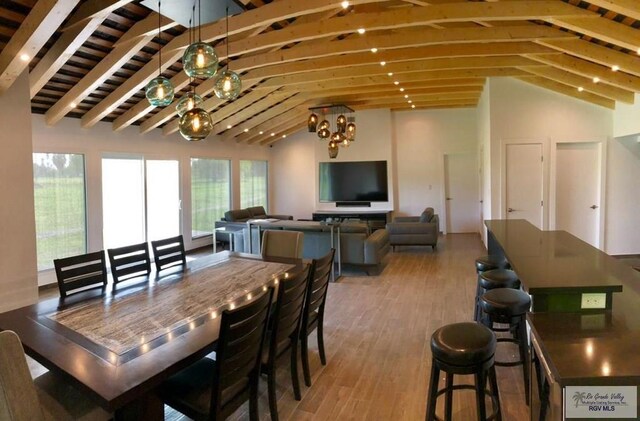 dining space with hardwood / wood-style floors, vaulted ceiling with beams, and a chandelier