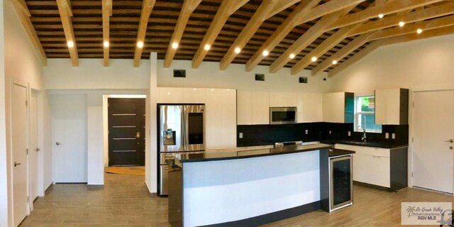 kitchen featuring appliances with stainless steel finishes, beverage cooler, high vaulted ceiling, a center island, and white cabinetry