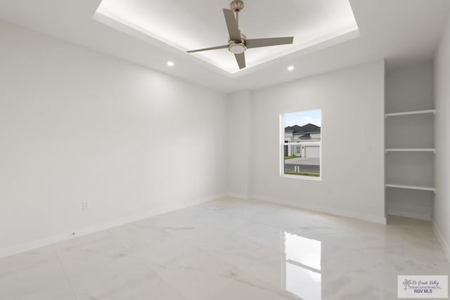 unfurnished room featuring a tray ceiling, built in shelves, and ceiling fan