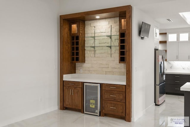 bar featuring decorative backsplash, stainless steel refrigerator, and beverage cooler