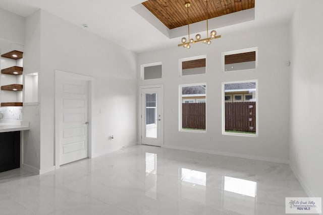 interior space with a raised ceiling, wood ceiling, a high ceiling, and an inviting chandelier