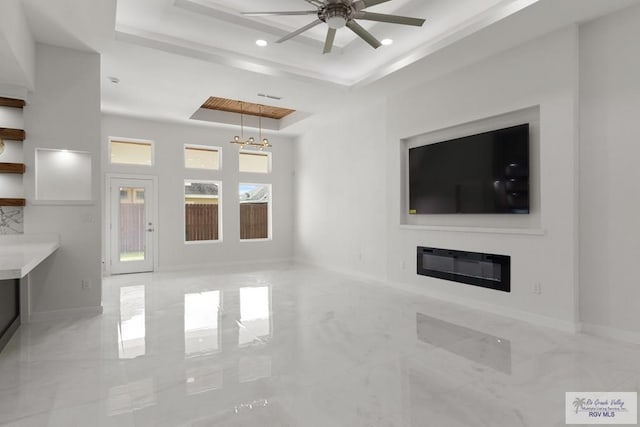 unfurnished living room featuring ceiling fan with notable chandelier and a tray ceiling