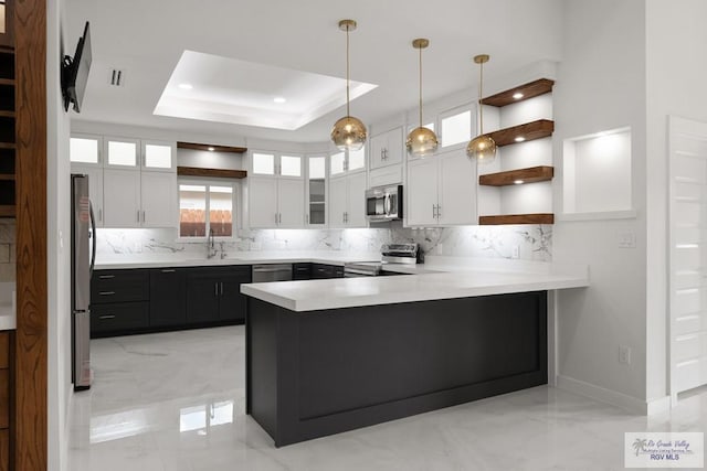 kitchen featuring white cabinets, hanging light fixtures, appliances with stainless steel finishes, a tray ceiling, and kitchen peninsula