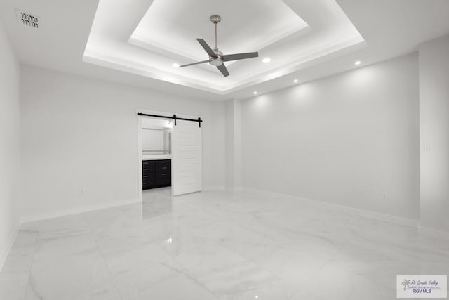 interior space featuring a raised ceiling, a barn door, and ceiling fan