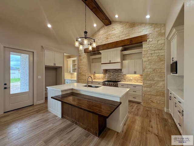 kitchen featuring vaulted ceiling with beams, white cabinetry, a center island with sink, and decorative light fixtures