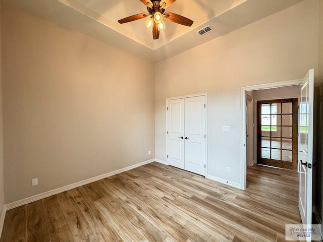 unfurnished bedroom featuring light hardwood / wood-style flooring, a raised ceiling, and ceiling fan