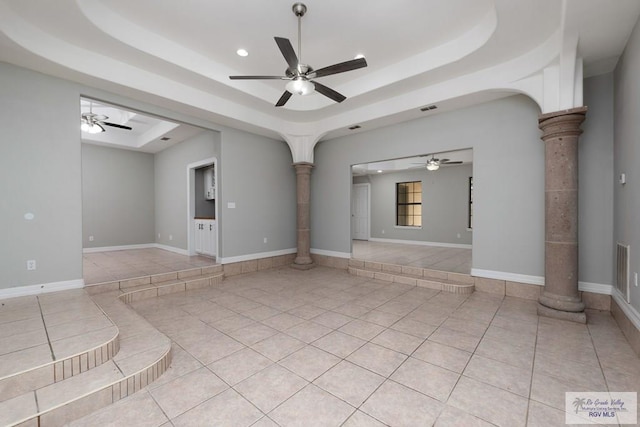 spare room with arched walkways, a raised ceiling, a ceiling fan, ornate columns, and light tile patterned flooring