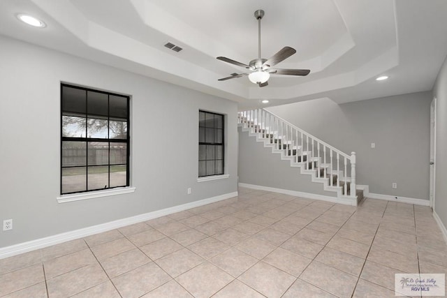 spare room featuring light tile patterned floors, baseboards, a raised ceiling, a ceiling fan, and stairway