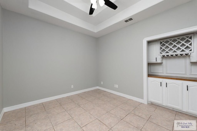 spare room featuring light tile patterned floors, a raised ceiling, visible vents, and baseboards