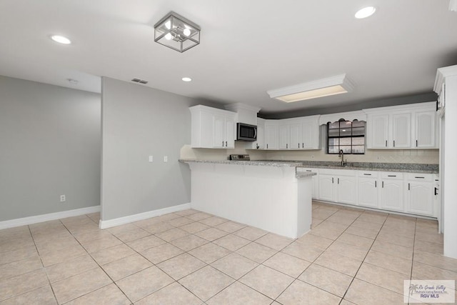 kitchen featuring light tile patterned floors, stainless steel microwave, a peninsula, white cabinetry, and a sink