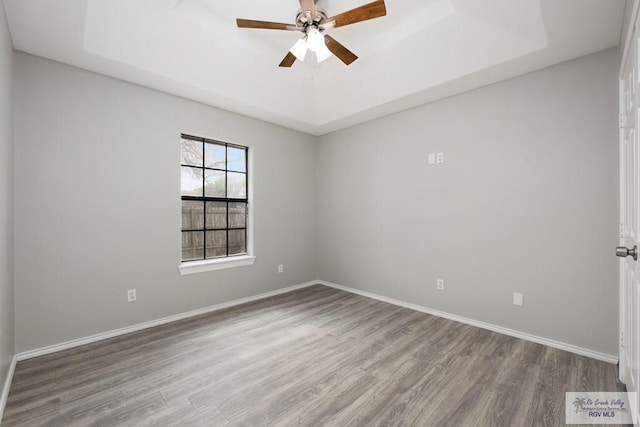 unfurnished room featuring a tray ceiling, wood finished floors, a ceiling fan, and baseboards