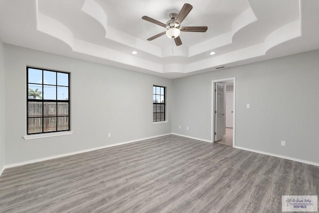 unfurnished room featuring light wood-style flooring, a tray ceiling, and baseboards