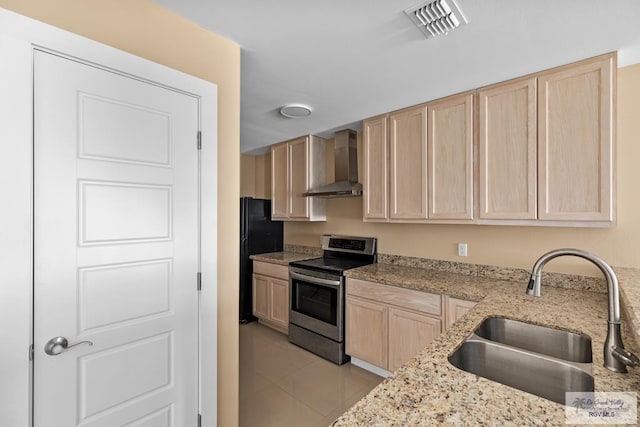 kitchen featuring light brown cabinetry, sink, stainless steel range with electric stovetop, black fridge, and wall chimney exhaust hood