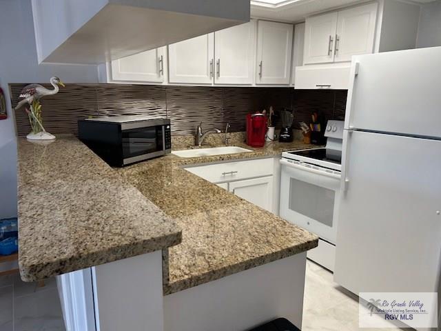 kitchen with white appliances, kitchen peninsula, and white cabinets