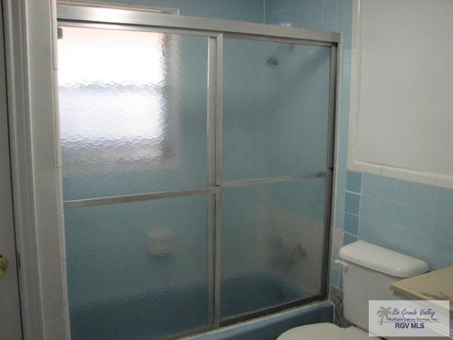 full bath featuring toilet, shower / bath combination with glass door, and tile walls