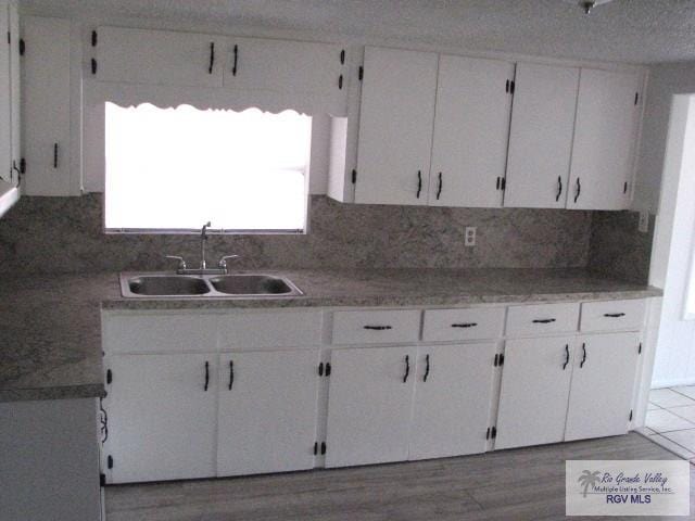 kitchen featuring white cabinets, decorative backsplash, a sink, and wood finished floors