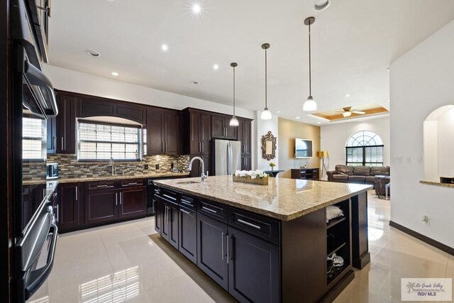 2360 Deer Run Cir, Brownsville, TX 78521 - kitchen with freestanding refrigerator, decorative backsplash, a kitchen island with sink, a ceiling fan, and light stone countertops