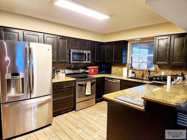 kitchen with appliances with stainless steel finishes, sink, backsplash, and light stone counters